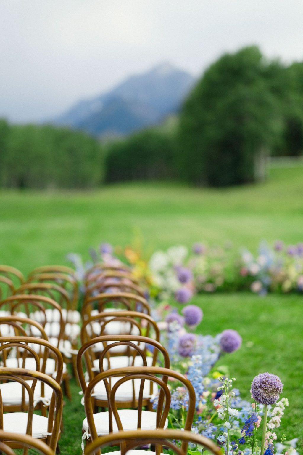 A wildflower wedding at T Lazy 7 Ranch, Aspen: bentwood ceremony chairs beside a low border of meadow flowers