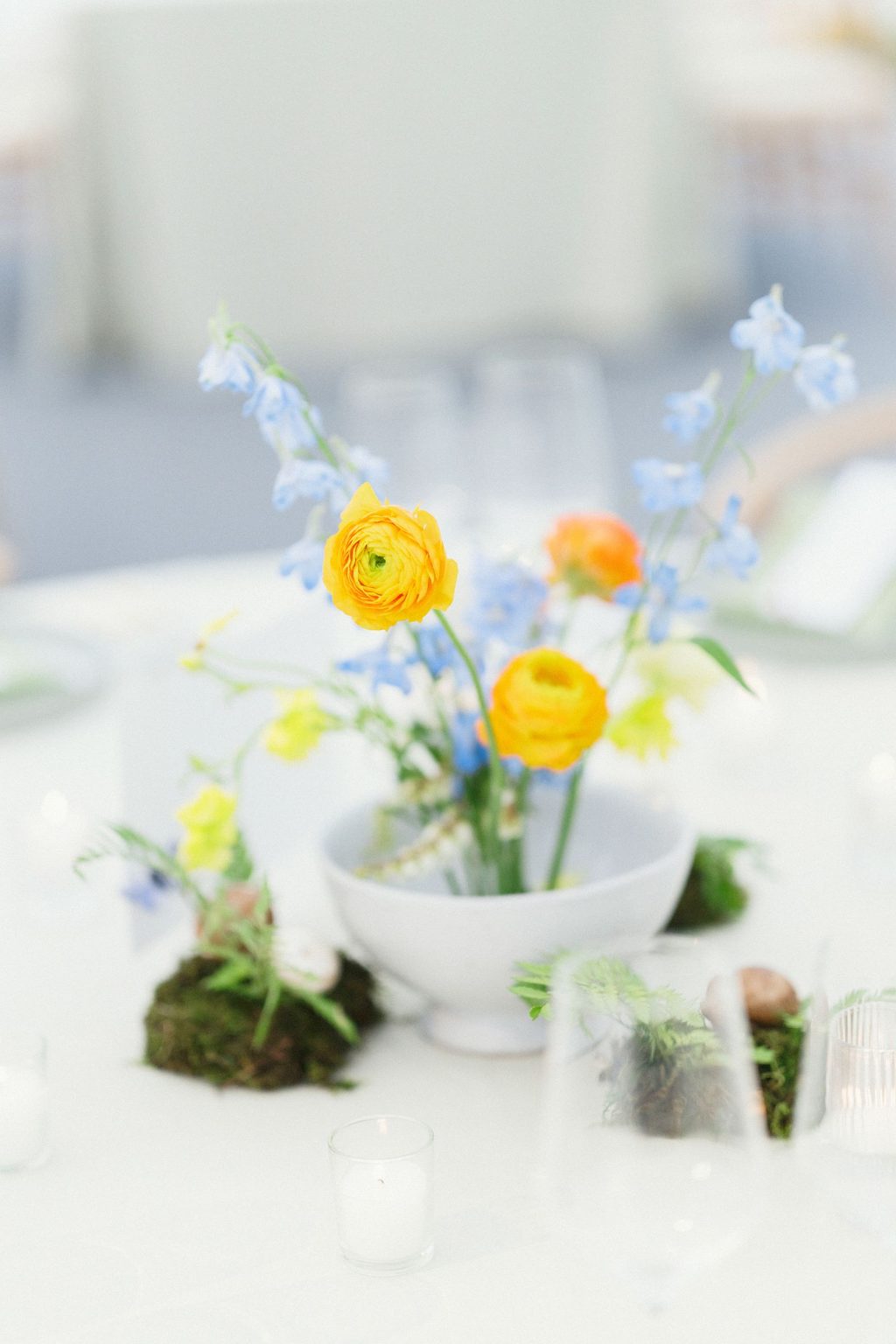 A wildflower wedding at T Lazy 7 Ranch, Aspen: ranunculus and delphinium in a low white vessel with moss