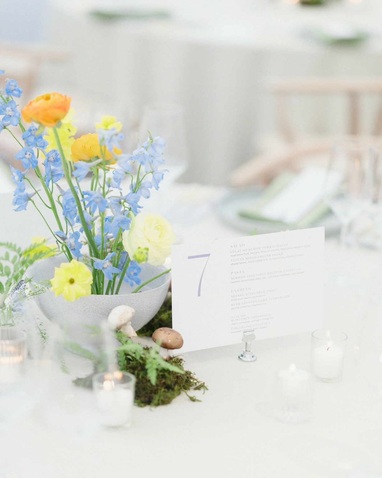 A wildflower wedding at T Lazy 7 Ranch, Aspen: a centerpiece of ranunculus, delphinium, and moss beside a table number